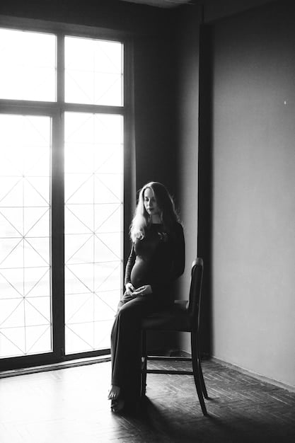 A black and white photography featuring a silhouette of a pregnant woman holding her belly, set against a softly lit background, symbolizing motherhood and the anticipation of new life.