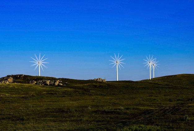 Wind turbines on a green hill with a clear blue sky, representing clean energy and environmental protection.