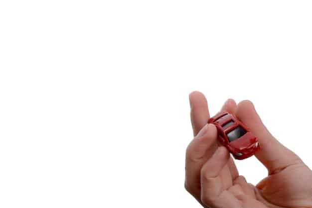 A close-up of a hand holding a car key with a small calculator and a miniature house in the background, symbolizing the financial decisions involved in buying a car.