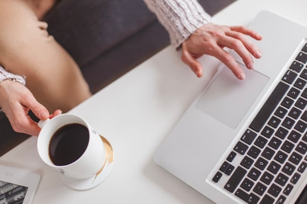 Close-up of a person's hands typing on a laptop keyboard, with a cup of coffee and a notebook on the desk, in a brightly lit home office.