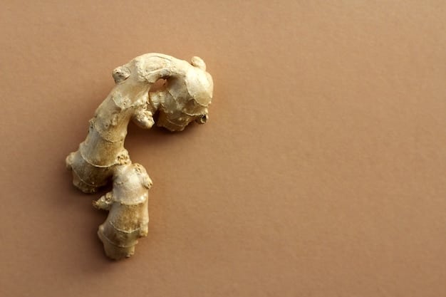 An overhead shot of sliced ginger root, showcasing its textured surface and warm yellow hue. A cup of steaming ginger tea sits beside the slices, with a spoon resting on the side. The background is a minimalist wooden surface.