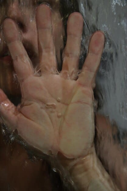A detailed photo focusing on the process of applying cool, running water to a minor burn on a person's hand. The water stream is gentle, and the skin around the burn appears slightly red.